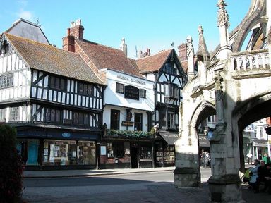 Half timbered buildings and shops next to an old stone archway in a town square at Rojoy Salisbury