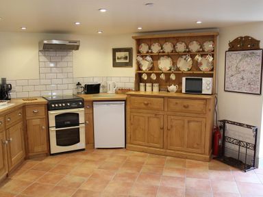 A kitchen with wooden cabinets a stove a fridge a microwave and plates on a wooden rack at The Folly at Castlebridge in Mere