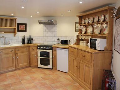 A kitchen with wooden cabinets a stove a small refrigerator a microwave and a wooden cupboard with plates and mugs at The Folly at Castlebridge in Mere