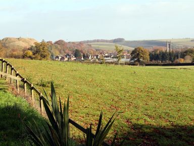 A green field with a wooden fence and a town in the distance with hills and trees at The Folly at Castlebridge in Mere