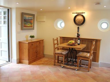 A dining area with a wooden table and two chairs with cushions a wooden cabinet and wall art at The Folly at Castlebridge in Mere