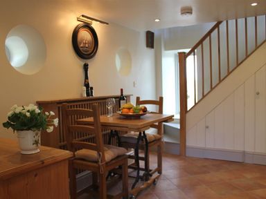 A dining area with a wooden table and chairs a fruit plate and a bottle of wine under stairs at The Folly at Castlebridge in Mere