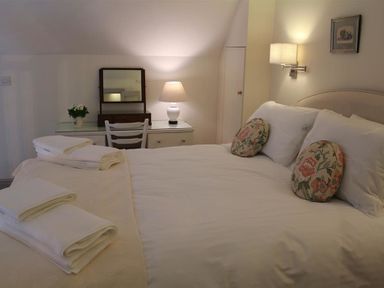A bedroom with a bed with white linens and floral cushions two stacks of folded towels a desk with a lamp a mirror and a chair at The Folly at Castlebridge in Mere