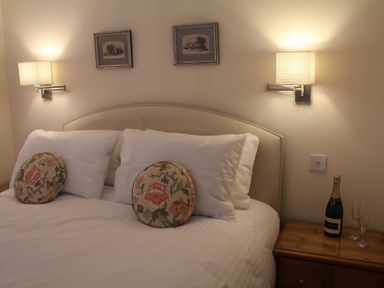 A bedroom with a bed with floral round pillows and white lamps on the wall at The Folly at Castlebridge in Mere