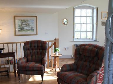 A sitting area with two plaid armchairs a small round wooden table with a plant a window and a framed picture on the wall at The Folly at Castlebridge in Mere