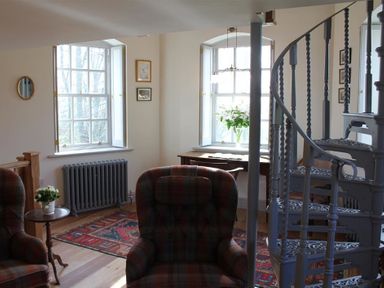 A sitting area with plaid armchairs a small wooden table a patterned rug and a metal spiral staircase at The Folly at Castlebridge in Mere