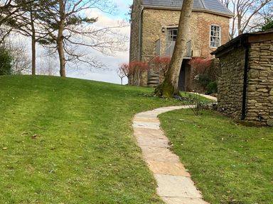A stone pathway through a grassy area leading to a stone house with a balcony and spiral staircase at The Folly at Castlebridge in Mere