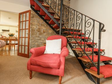 A living room with an armchair and staircase at Droop Farm Cottage in Droop near Hazelbury Bryan