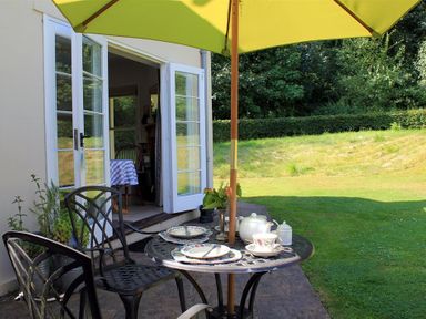 An outdoor patio with a black metal table and chairs set with plates cups and a teapot under a yellow umbrella at West Lodge in Rockbourne
