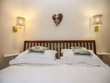 A double bed with two white pillows and decorative cushions under two wall lamps in a bedroom at West Lodge in Rockbourne