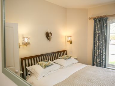 A bedroom with a wooden bed frame two pillows two wall lamps and floral curtains at West Lodge in Rockbourne