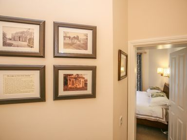 A hallway with four framed pictures on a wall and a partially open door leading to a bedroom at West Lodge in Rockbourne