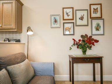 A small wooden table with a vase of leaves and flowers next to a gray couch and a floor lamp with framed animal pictures on the wall at West Lodge in Rockbourne