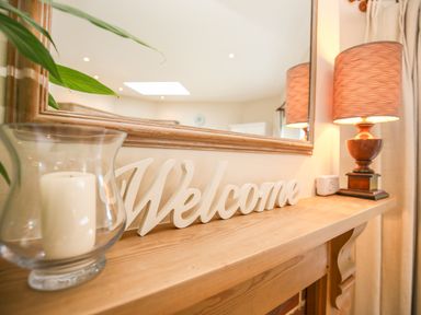 A wooden shelf with a candle in a glass holder a welcome sign and a lamp at West Lodge in Rockbourne