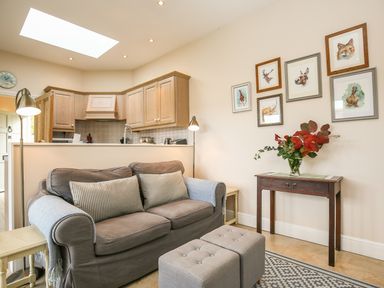 A living room with a sofa and ottomans next to a console table with flowers and framed animal pictures on the wall at West Lodge in Rockbourne