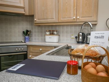 A kitchen countertop with a basket of bread, a basket of eggs, a jar of jam, a folder, and a welcome note at West Lodge in Rockbourne