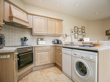 A kitchen with wooden cabinets a built-in oven a sink a dishwasher and a washing machine at West Lodge in Rockbourne