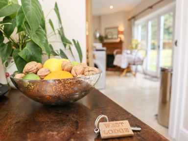 A bowl of fruit and nuts on a wooden surface with a plant and a keychain labeled West Lodge in Rockbourne
