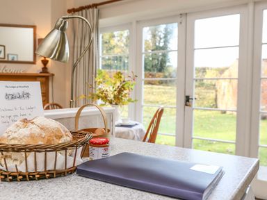 A kitchen counter with a basket of bread and jam jar near a lamp and glass doors leading to a garden at West Lodge in Rockbourne