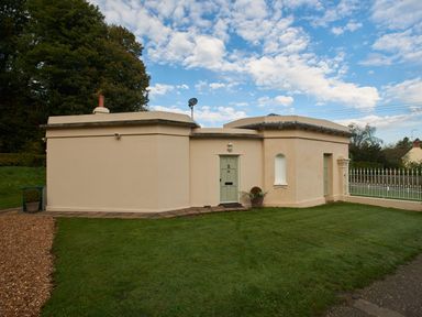 A small beige building with two green doors and a grassy lawn at West Lodge in Rockbourne
