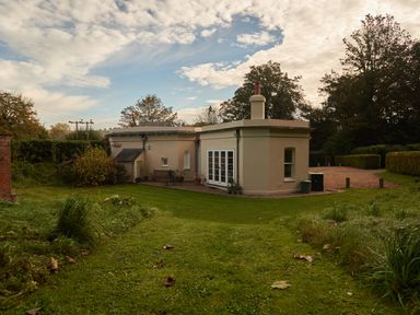 A backyard with a grass lawn and a beige house with white doors and windows at West Lodge in Rockbourne