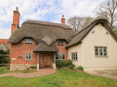 A cottage with a thatched roof brick walls and a wooden door surrounded by grass at Cosy Cot in Stapleford