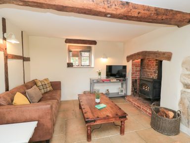 A living room with a brown sofa a wooden coffee table a wood burning stove and a television on a gray console at Cosy Cot in Stapleford