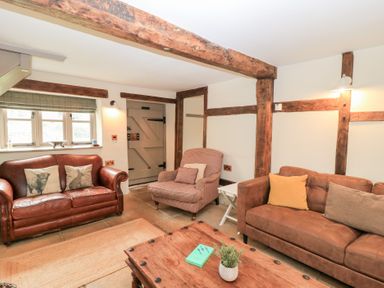 A living room with two sofas an armchair a wooden coffee table and exposed wooden beams at Cosy Cot in Stapleford
