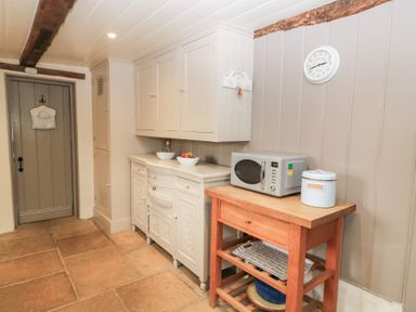 A kitchen corner with cabinets a wooden table microwave and a clock on the wall at Cosy Cot in Stapleford