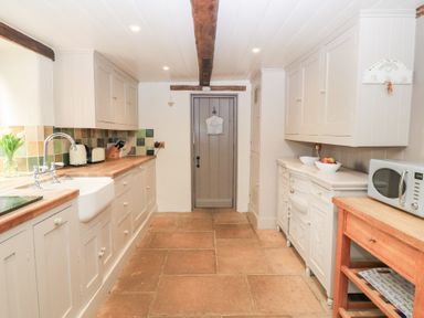 A kitchen with wooden countertops cabinets a farmhouse sink a microwave on a wooden table and a door at the end of the room at Cosy Cot in Stapleford