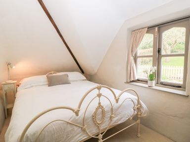 A bedroom with a metal bed frame a bedside table with a lamp and a window with curtains and a potted plant at Cosy Cot in Stapleford