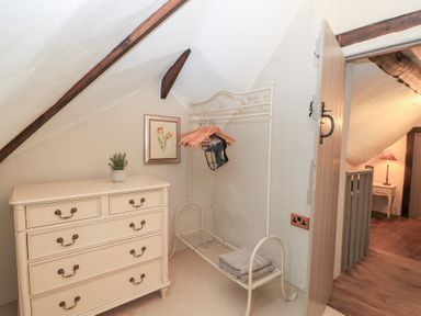 A small room with a cream chest of drawers a metal clothes rack with hangers folded towels and a framed flower picture at Cosy Cot in Stapleford