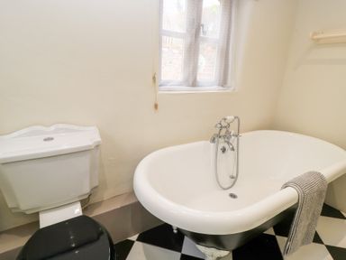 A bathroom with a freestanding clawfoot bathtub a toilet with a black seat and a window at Cosy Cot in Stapleford