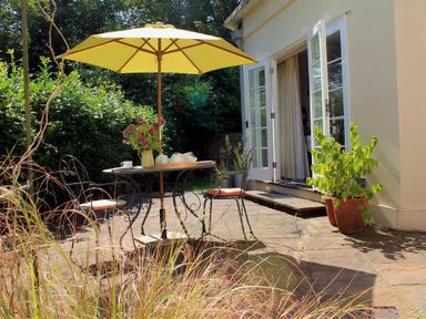A patio with a table and chairs under a yellow umbrella outside a building with open glass doors and potted plants at East Lodge in Rockbourne