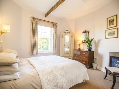 A bedroom with a double bed a window with plaid curtains a wooden dresser with a mirror and a potted plant at East Lodge Rockbourne