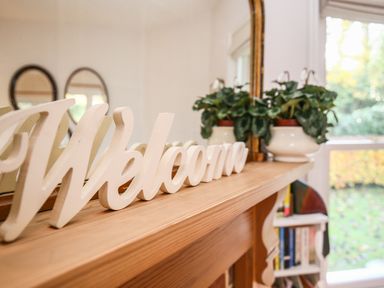 A welcome sign on a wooden mantelpiece with a potted plant and a mirror in a room at East Lodge in Rockbourne