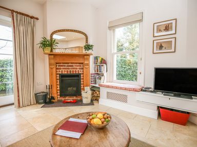 A living room with a fireplace a window seat a television and a round wooden table with a fruit bowl at East Lodge Rockbourne