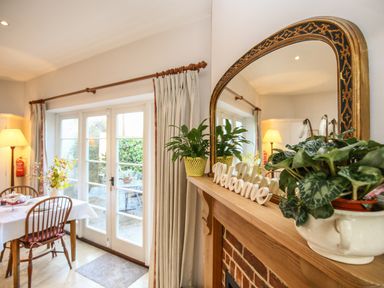 A dining room with a table and chairs next to glass doors and a wooden mantel with plants and a welcome sign at East Lodge Rockbourne