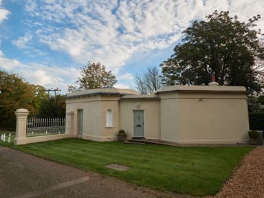 A single story house with beige walls green door and lawn in front at East Lodge in Rockbourne