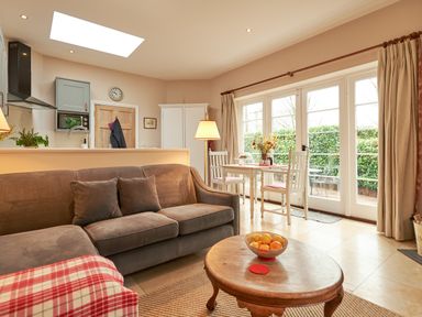 A living room with a brown sofa and round wooden coffee table next to a dining table by glass doors at East Lodge in Rockbourne