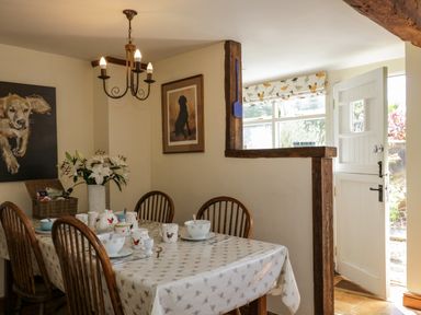 A dining area with a table set with cups bowls and plates and wooden chairs near an open door at Henmarsh Cottage in Moreton-In-Marsh