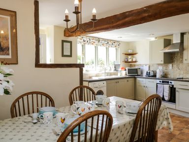 A kitchen and dining area with a table set for breakfast and wooden chairs at Henmarsh Cottage in Moreton-In-Marsh