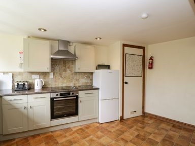 A kitchen with tiled floor white cabinets oven refrigerator toaster kettle and fire extinguisher on wall at Henmarsh Cottage in Moreton-In-Marsh