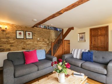 A living room with two grey sofas and a wooden coffee table with flowers at Henmarsh Cottage in Moreton-In-Marsh
