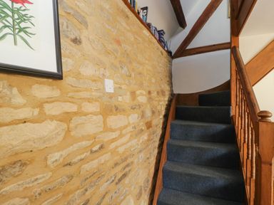 A carpeted staircase with a wooden bannister next to a stone wall at Henmarsh Cottage in Moreton-In-Marsh