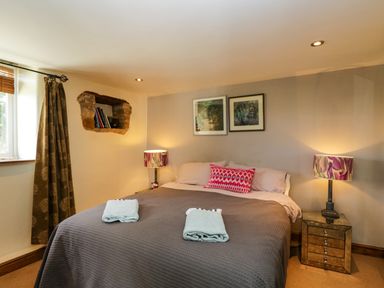 A bedroom with a double bed two bedside tables with lamps two folded towels on the bed and framed pictures on the wall at Henmarsh Cottage in Moreton-In-Marsh