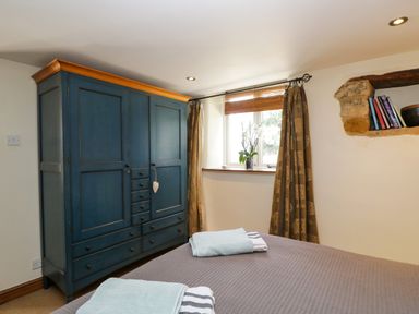 A bedroom with a blue wardrobe a window with curtains and folded towels on a bed at Henmarsh Cottage in Moreton-In-Marsh
