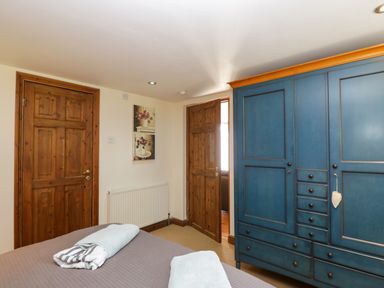 A bedroom with a bed, a blue wardrobe, wooden doors, and two paintings on the wall at Henmarsh Cottage in Moreton-In-Marsh