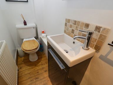 A bathroom with a toilet with a wooden seat and a sink with a tiled backsplash at Henmarsh Cottage in Moreton-In-Marsh