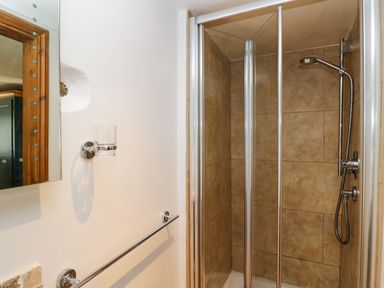 A bathroom shower area with tiled walls glass door a showerhead towel rail and a glass holder at Henmarsh Cottage in Moreton-In-Marsh